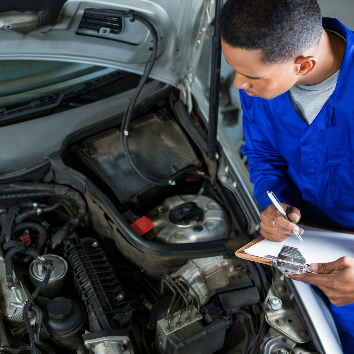 ASE-certified mechanic inspecting a car engine and taking notes on a clipboard at a Sarasota auto repair shop