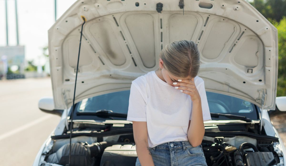 Frustrated woman standing in front of a broken down car with the hood open — the cost of skipping vehicle maintenance in Sarasota